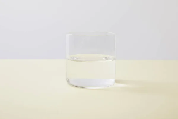Склянка Водою Жовтій Поверхні Ізольовані Сірому — стокове фото