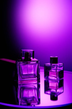 Violet perfume bottles on round mirror surface and light spot on background clipart