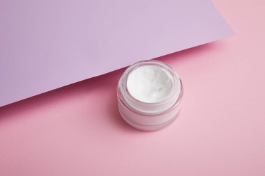 Cam kavanozda pembe ve leylak arkaplanlı kozmetik kremi 