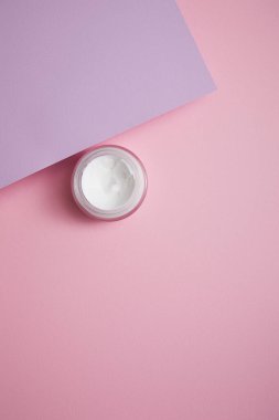 Cam kavanozda pembe ve leylak arkaplanda kozmetik kremin üst görüntüsü 