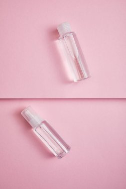 Top view of transparent sanitizer spray and lotion bottle with liquid on pink background clipart