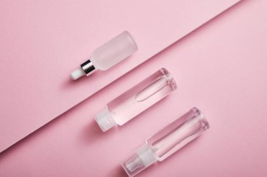 Kozmetik şişesi, spreyi ve pembe arka planda sıvı bulunan serum şişesiyle düz yatıyordu.