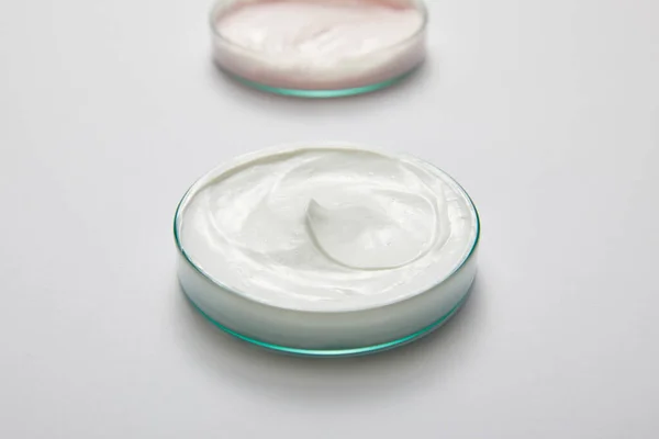 グレーの背景に白とピンクの化粧品クリームと実験室のガラス製品の選択的な焦点 — ストック写真