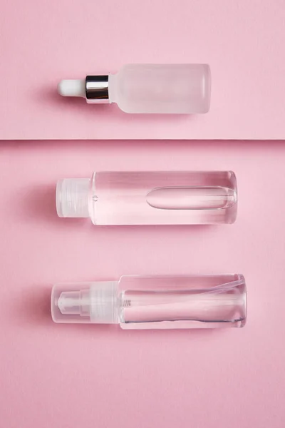 在粉色和灰色背景下 平铺着化妆品瓶 喷雾和血清 — 图库照片