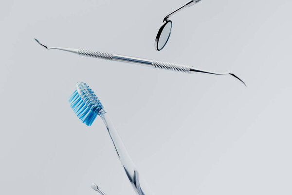 Dental instruments and toothbrush with blue bristles levitating isolated on grey background