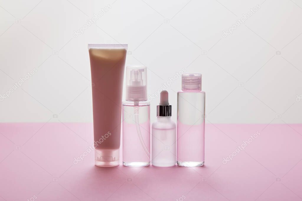 Set of cosmetic bottles and cosmetic cream tube on pink and grey background