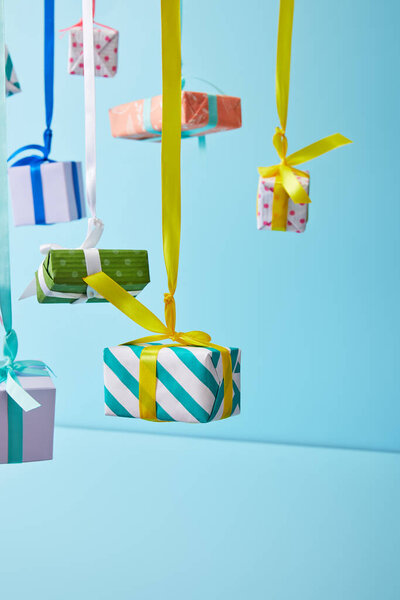 festive colorful gift boxes hanging on ribbons on blue background