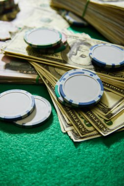 Yeşil arka planda dolar banknotları ve kumarhane fişleri seçici odak