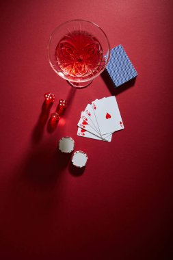 Oyun kartları, kumarhane fişleri ve kırmızı arka plandaki zar yakınlarındaki kokteyl kadehinin üst görüntüsü