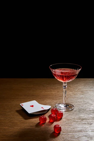 在木制表面的卡片和骰子旁边的酒杯 用黑色隔开 — 图库照片
