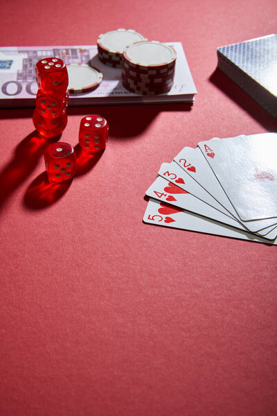 High angle view of playing cards, dice, casino chips and money on red