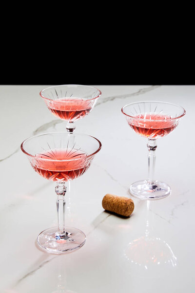 Glasses of cocktail and cork on white surface isolated on black