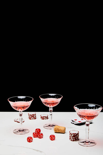 Glasses of cocktail, dice, cork, casino tokens and pack of cards on white surface isolated on black