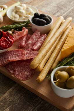 Tahtaya yüksek açılı tahta, salam dilimleri ve ahşap arka planda antipasto malzemeleri.