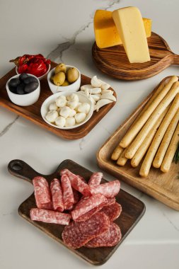 Ekmek çubukları, salam dilimleri, peynir ve beyaz üzerine antipasto malzemesi olan yüksek açılı tahtalar.