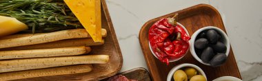 Ekmek çubuklarının, peynirin, yeşilliğin ve panoların üzerinde antipasto içerikleri olan beyaz panoramik çekimin en üst görüntüsü.