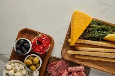 Salam dilimleri, ekmek çubukları, peynir, yeşillik ve beyaz arka planda panolarda antipasto içerikleri olan kaseler.