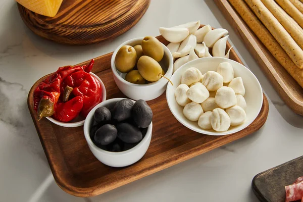 用面包棒 橄榄碗 莫扎拉和腌制辣椒在白色上的高角形木板 — 图库照片