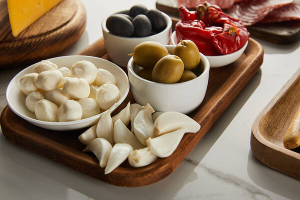 High angle view of boards with garlic and bowls with olives, mozzarella and marinated chili peppers on white