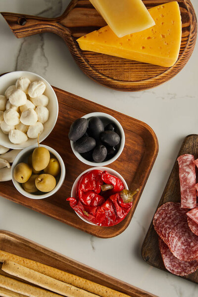 Top view of boards with cheese, salami slices and antipasto ingredients on white