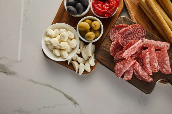 Top view of salami slices with antipasto ingredients on boards on white