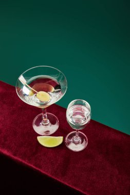 Yüksek açılı cam ve kokteyl bardağı vermut, limon dilimi ve kadife kürdanlı zeytin yeşil yüzeyde izole edilmiş.
