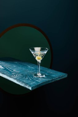 cocktail glass with vermouth and whole olive on toothpick on blue wooden surface on geometric background clipart
