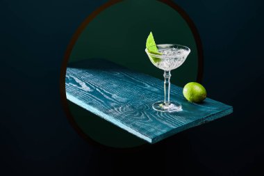 high angle view of cocktail glass with mint leaf and whole lime on blue wooden surface on geometric background clipart