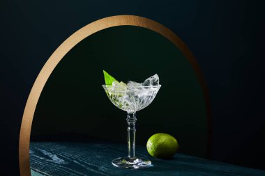 cocktail glass with mint leaf and whole lime on blue wooden surface on geometric background with golden circle clipart