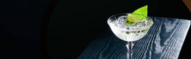 Buzlu kokteyl camının yüksek açılı görüntüsü ve siyah arkaplanda mavi ahşap yüzey üzerinde nane yaprağı.