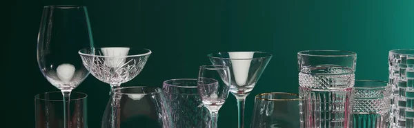 stock image panoramic view of old fashioned glass, cocktail glass, champagne flute, shot glass, highball glass, collins glass, brandy glass, cognac balloon and collins glass isolated on green