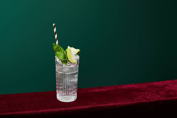 High angle view of mojito with ice, mint, lime and striped drinking straw in collins glass isolated on green