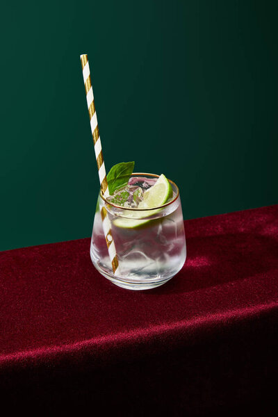 high angle view of old fashioned glass with golden rim with mojito and striped drinking straw isolated on green