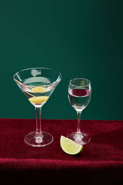 High angle view of shot glass and cocktail glass with vermouth, lime and whole olive on toothpick isolated on green