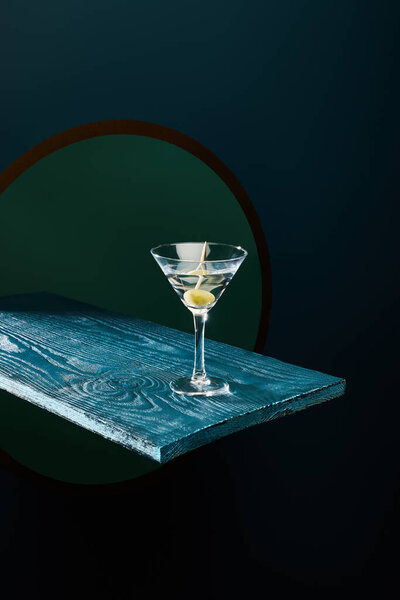 cocktail glass with vermouth and whole olive on toothpick on blue wooden surface on geometric background