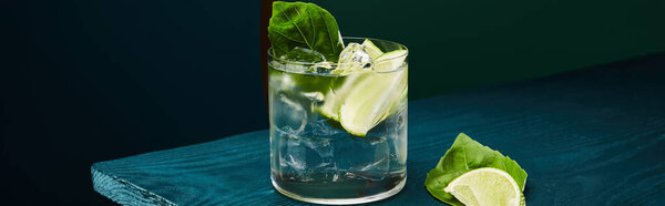 панорамный вид на старомодный стакан со свежим напитком, мятным листом и ломтиком лайма на голубой деревянной поверхности на зеленом и голубом геометрическом фоне
