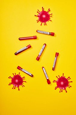 Coronavirus test harfleriyle test tüplerinin üst görüntüsü ve sarı üzerine virüsü çizmiş.