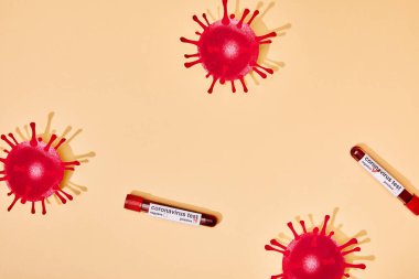 Coronavirus test harfleri bej üzerine yazılmış test tüplerinin yakınındaki çizilmiş virüsün üst görüntüsü 