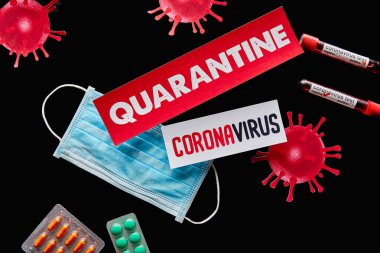Tıbbi maske, haplar ve koronavirüs testli test tüplerinin yanında karantina ve koronavirüs harfleri bulunan kağıtların üst görüntüsü siyah üzerinde izole edildi. 