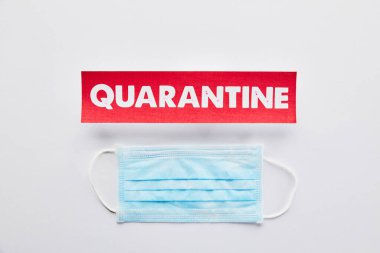 top view of paper with quarantine lettering near medical mask on white  clipart