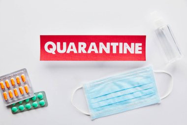 Tıbbi maske, hap ve el dezenfektanının yanında karantina harfleri olan kağıt üst görünümü 