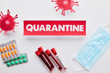 Karantina harflerinin olduğu kağıdın üst görüntüsü virüsün yanında, koronavirüs testli test tüpleri, tıbbi maske ve beyaz üzerine haplar. 