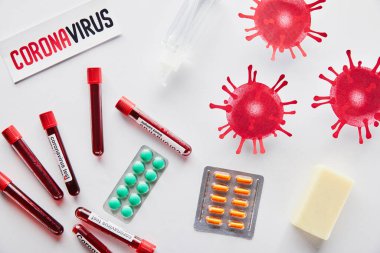 Coronavirus harfli kağıdın üst görüntüsü virüsün yanında, test tüpleri, el dezenfektanı, sabun çubuğu ve beyaz üzerine haplar. 
