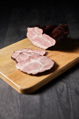 selective focus of tasty ham sliced ham on cutting board on wooden grey table clipart