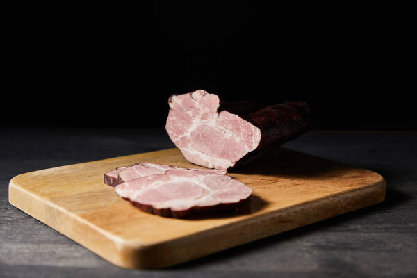 selective focus of tasty ham sliced ham on cutting board on wooden grey table isolated on black