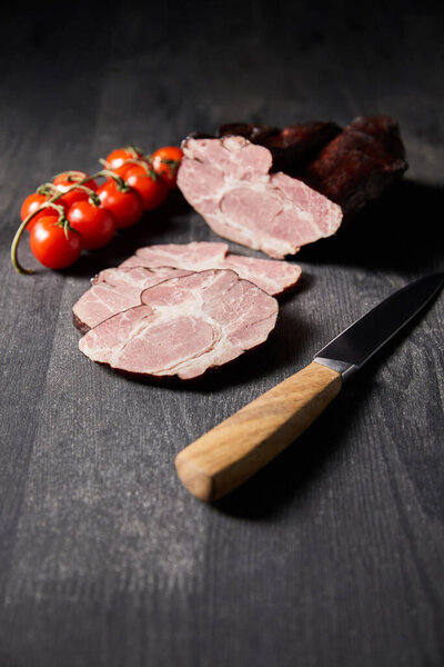 selective focus of tasty ham sliced ham, cherry tomatoes, knife on wooden grey table