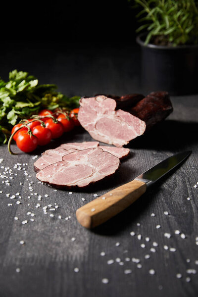 selective focus of tasty ham sliced ham, cherry tomatoes, parsley, salt, knife on wooden grey table