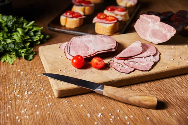 Selective focus of tasty ham slices, cherry tomatoes and knife on cutting board near parsley and canape — Stock Image Selective Focus Tasty Ham Slices Cherry Tomatoes Knife Cutting Board Royalty Free Stock Photos
