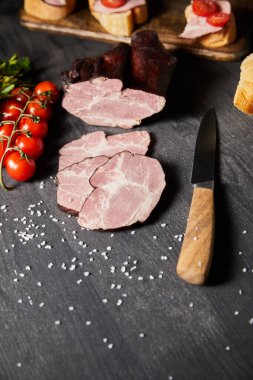 Lezzetli jambon dilimlenmiş domuz eti, kiraz domatesleri, maydanoz, tuz, bıçak ve baget.