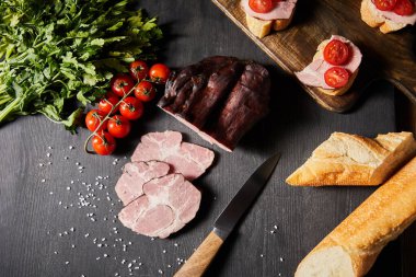 Lezzetli jambon dilimlenmiş domuz eti, kiraz domatesleri, maydanoz, tuz, bıçak ve ekmek.